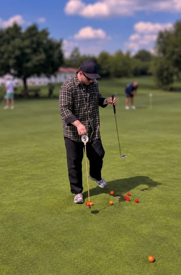 Golfer sammelt auf dem Putting-Grün orange Bälle an Loch 5 ein.